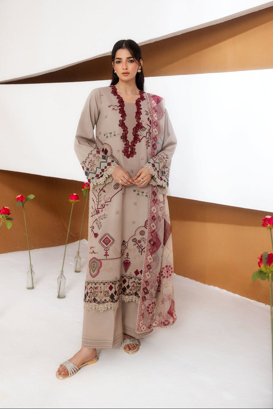 A woman models a beige three-piece ethnic suit with maroon and multicolor embroidery, standing in a modern studio setting with white walls and brown accents.
