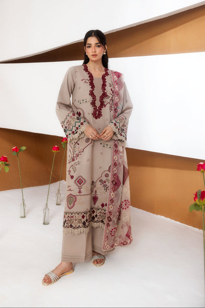 A woman models a beige three-piece ethnic suit with maroon and multicolor embroidery, standing in a modern studio setting with white walls and brown accents.