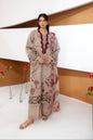 A woman models a beige three-piece ethnic suit with maroon and multicolor embroidery, standing in a modern studio setting with white walls and brown accents.